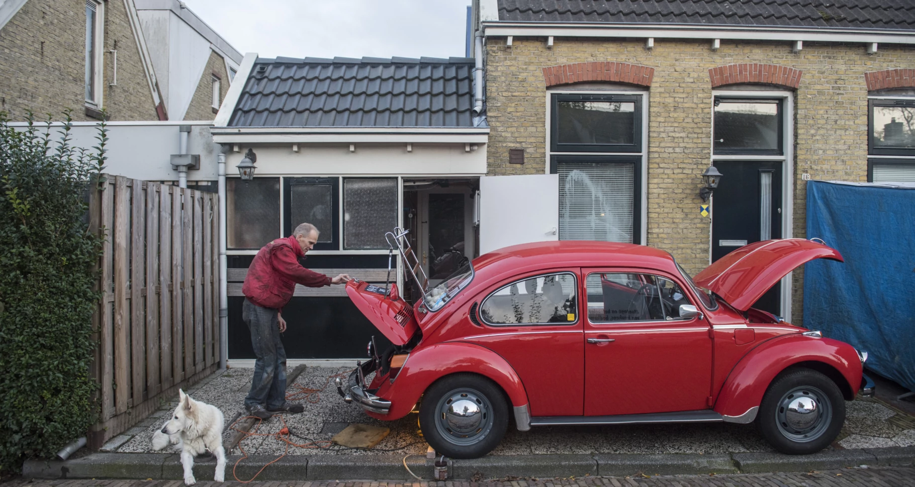 Man bij rode eend (auto) en witte herdershond in de Vlietzone